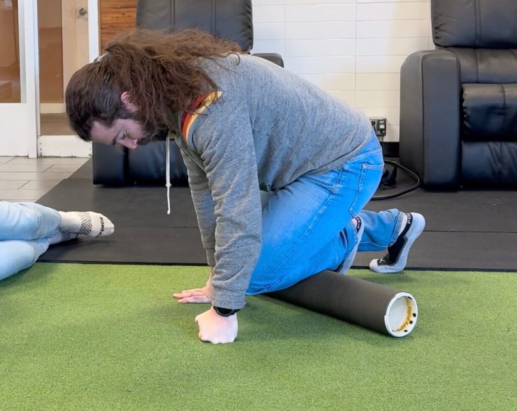 Dr. John showing how to foam roll the shin with the foam roller just to the outside of his bone. He is in table top position leaning to the outside.